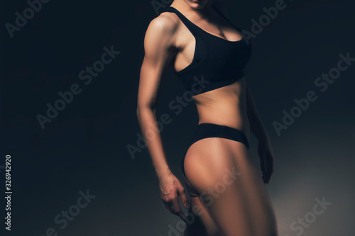 Sexy slim fit woman body. Muscled back. Sportswear. Dark background