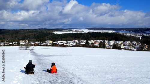 zwei Kinder starten zur Schlittenfahrt in herrlicher, sonniger Winterlandschaft im Schwarzwald
