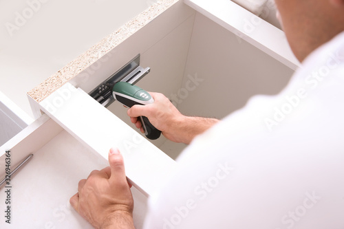 Worker installing kitchen furniture with electric screwdriver, closeup