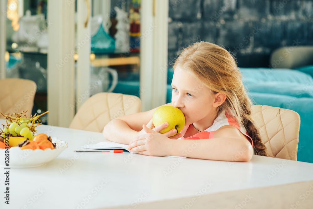 a little girl at the table with a notebook, doing homework and decided to eat a fresh Apple. a little girl at the table with a notebook, doing homework and decided to eat a fresh Apple.