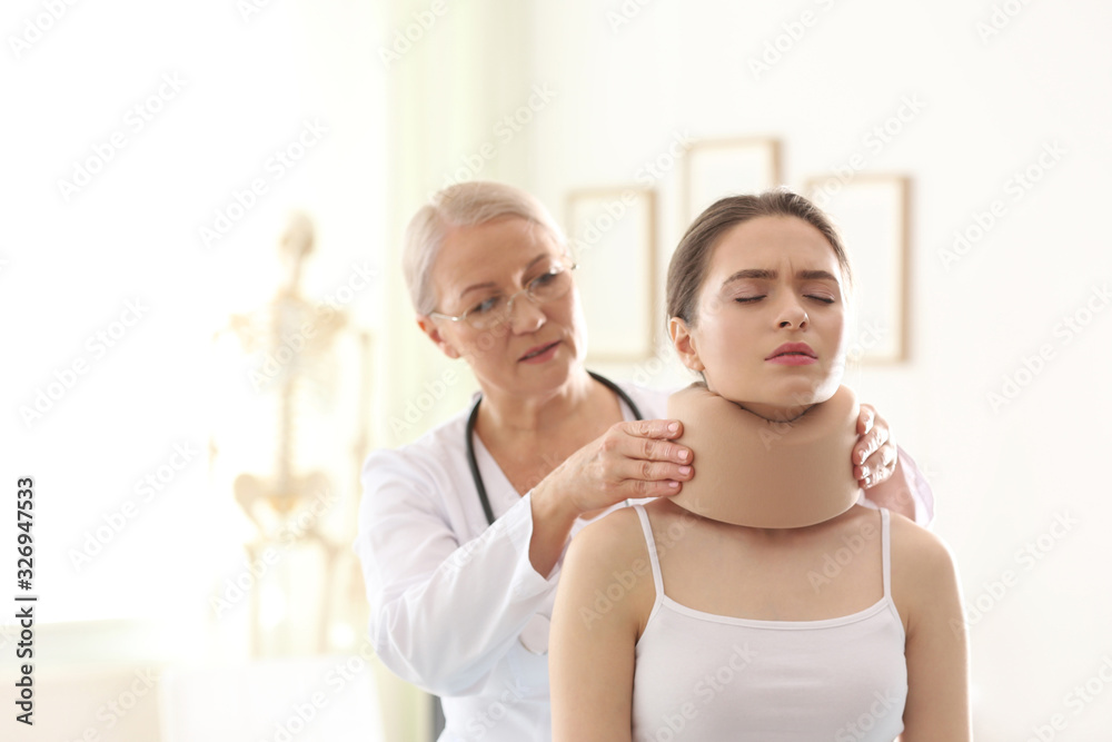 Fototapeta premium Female orthopedist applying cervical collar onto patient's neck in clinic