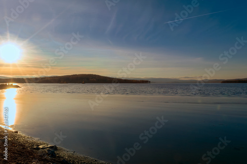 Summer landscape on the shore of a forest lake. Forest lake under blue cloudy sky.