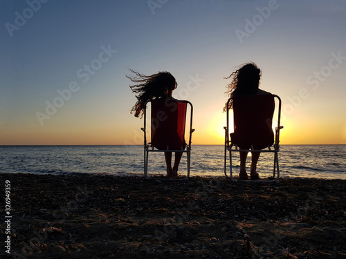 Two young girls watching the sunset at the beach.