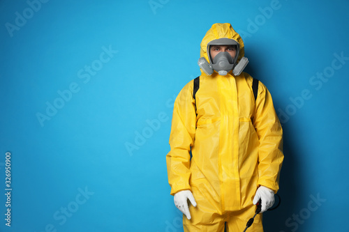 Man wearing protective suit with insecticide sprayer on blue background, space for text. Pest control photo