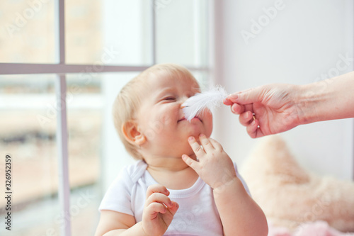 mother and daughter on the window tickles the nose with a white feather photo