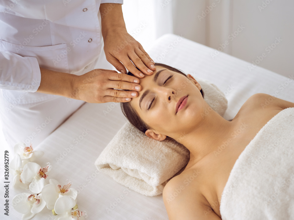 Beautiful brunette woman enjoying facial massage with closed eyes. Relaxing treatment in medicine and spa center concepts Beautiful brunette woman enjoying facial massage with closed eyes. Relaxing treatment in medicine and spa center concepts
