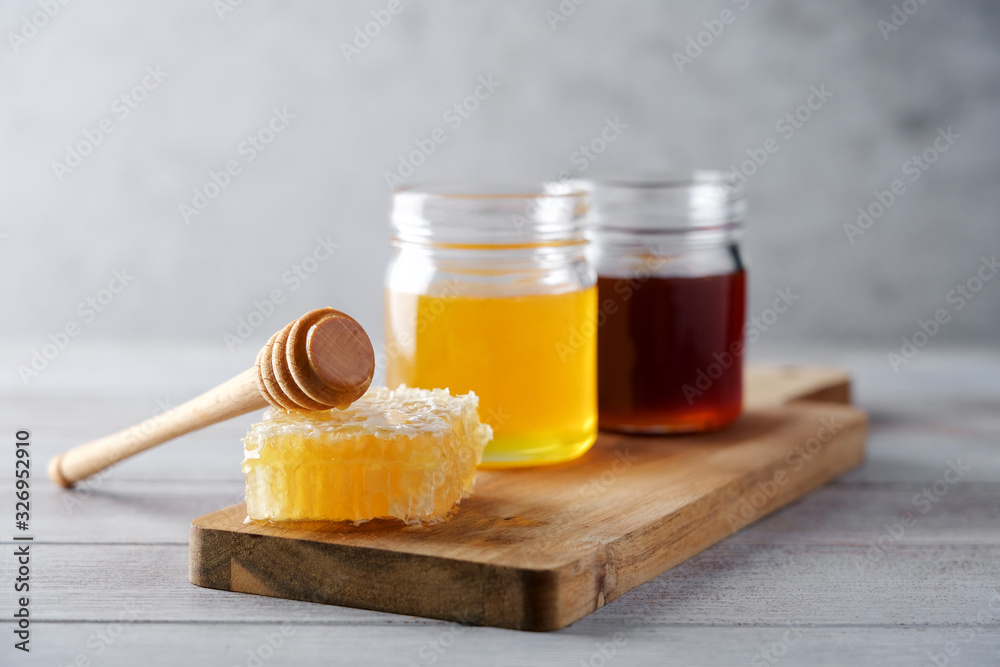Fresh honey and honeycombs on wooden cutting board. Light floral and dark honey in glass jars - obrazy, fototapety, plakaty 