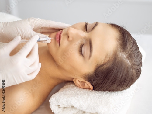 Beautician doing beauty procedure with syringe to face of young brunette woman. Cosmetic medicine and surgery, beauty injections