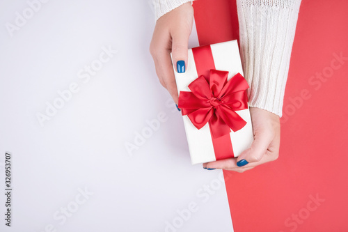 Gift box in women's hands on a gray red background © NS