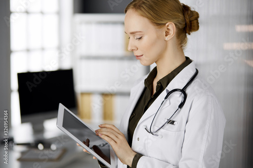 Cheerful smiling female doctor using tablet computer in clinic. Portrait of friendly physician woman at work. Perfect medical service in hospital. Medicine concept