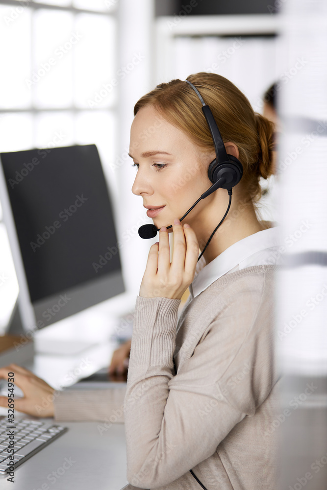 Businesswoman talking by headset while sitting in office. Call center and diverse people group in business Businesswoman talking by headset while sitting in office. Call center and diverse people group in business