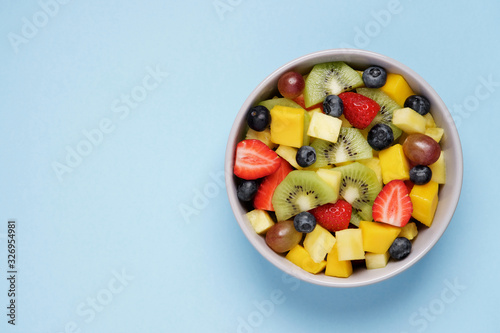 Fruit salad on bright blue background. Multi-colored ripe fruits and berries. Pineapple  mango  grape  strawberry  blueberry and kiwi