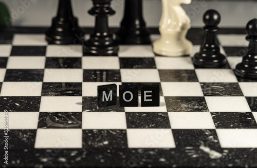 The concept of Moe represented by black and white letter tiles on a marble chessboard with chess pieces