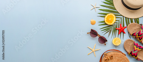 Top view summer banner with palm leaves and female beach accessories on a blue background. Rattan bag, sunglasses, hat and flip flops with copy space