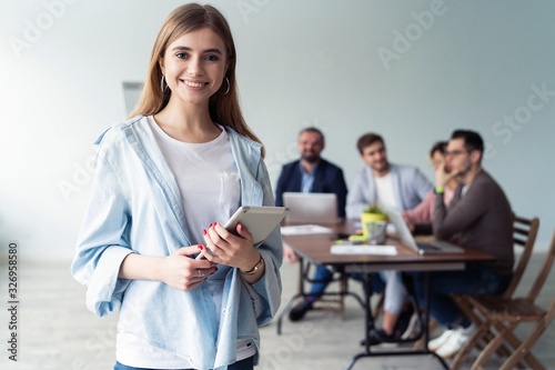 Beautiful young business lady looking at camera and smiling while her colleagues working in the background.