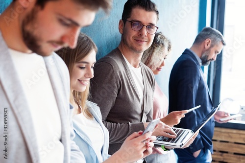 The connected team is an efficient team. Group of businesspeople using wireless technology together while standing in line against a blue background.