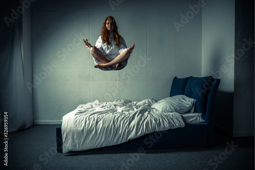 Obsessed girl levitating in lotus pose during meditation over bed photo