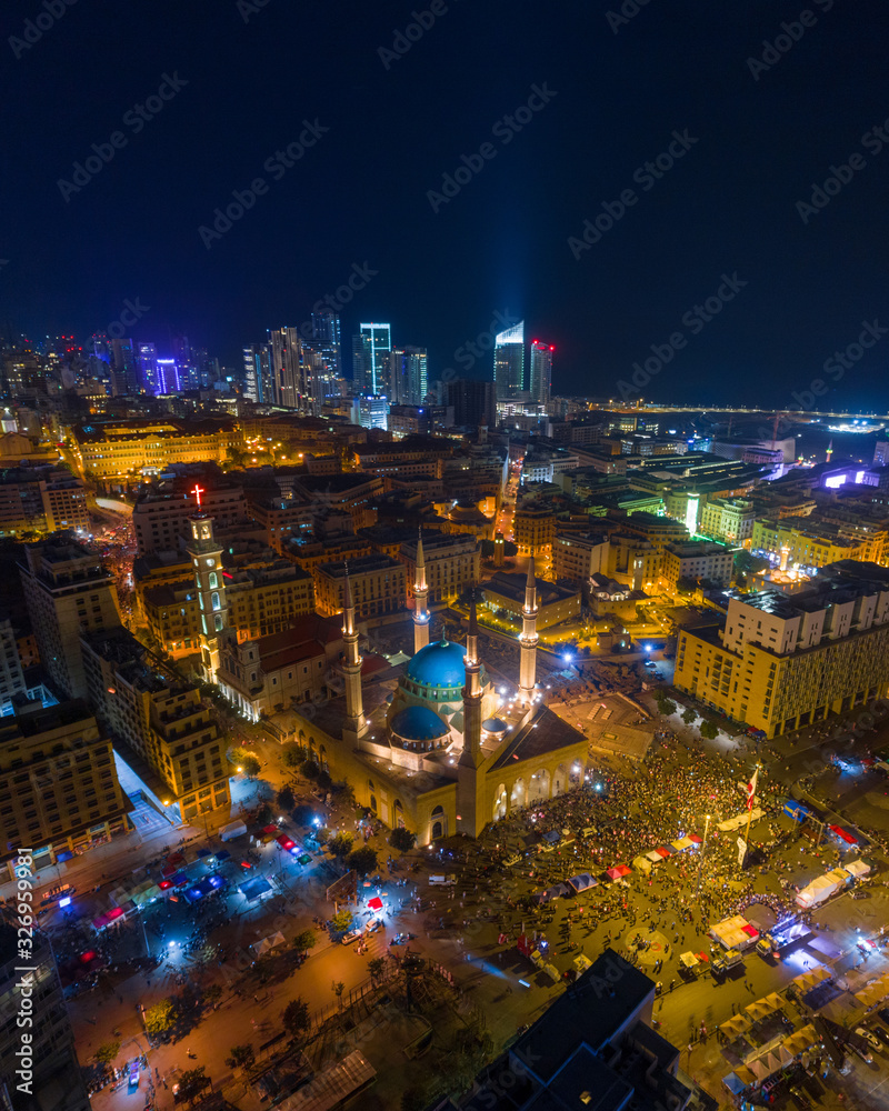 Fototapeta premium Beirut, Lebanon 2019: Aerial night drone shot of Beirut Downtown and skyline during the Lebanese revolution with hundreds of protesters in front of Mohammad Al Amin Mosque and St. George Church