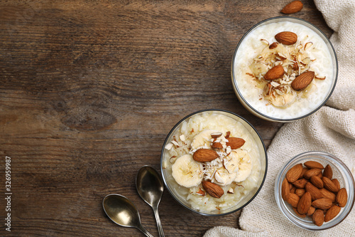 Delicious rice pudding with banana and almonds on wooden table, flat lay. Space for text