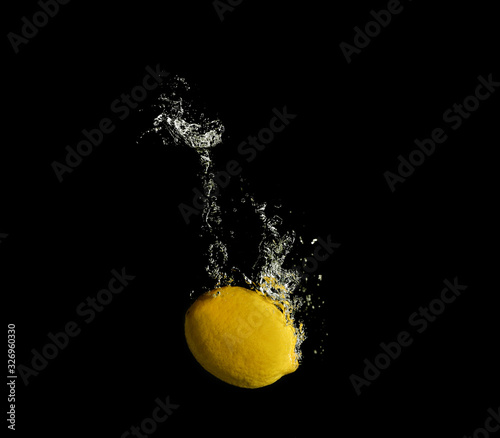 Ripe lemon falling down into clear water with splashes against black background