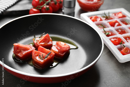 Melting ice cubes with tomatoes, oil and rosemary on grey table