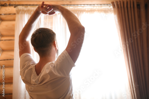 Man stretching near window indoors. Lazy morning