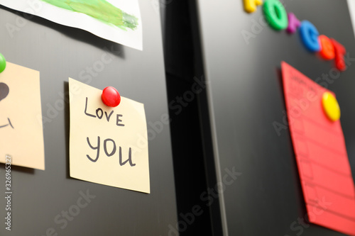 Note with phrase LOVE YOU and magnets on refrigerator, closeup