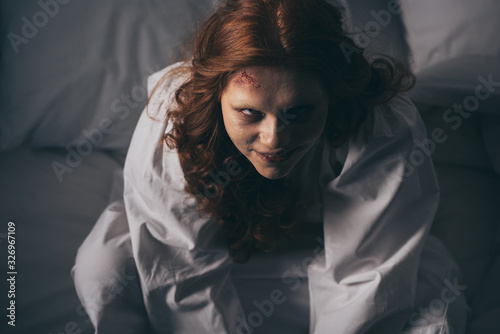 overhead view of demoniacal smiling woman in nightgown sitting in bed