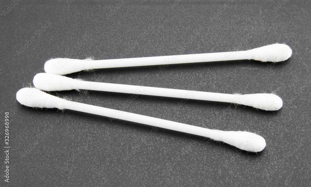 Three white plastic ear buds with soft white cotton on the end. On a black textured background. Hygiene and ear cleaning products. Three white plastic ear buds with soft white cotton on the end. On a black textured background. Hygiene and ear cleaning products.