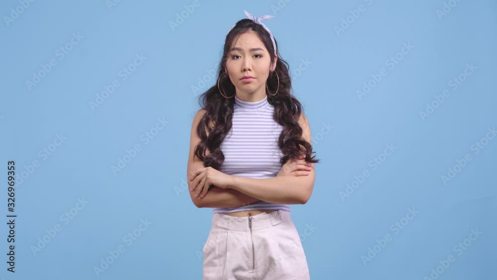 offended asian girl standing with crossed arms isolated on blue offended asian girl standing with crossed arms isolated on blue