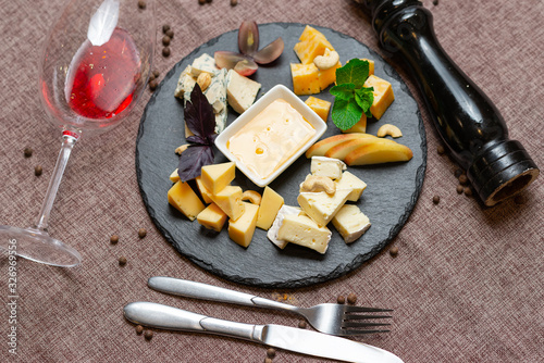 sliced cheese with honey, nuts, mint and a glass of red wine on a coffee color background