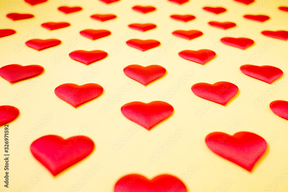 A lot of identical red silk hearts lying staggered on a yellow background. Symbol of love, tenderness and passion A lot of identical red silk hearts lying staggered on a yellow background. Symbol of love, tenderness and passion