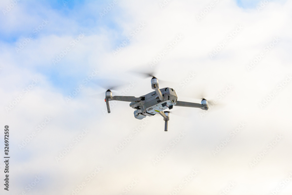 Small gray drone flying in the sky, quadcopter on a cloudy sky background. Small gray drone flying in the sky, quadcopter on a cloudy sky background.