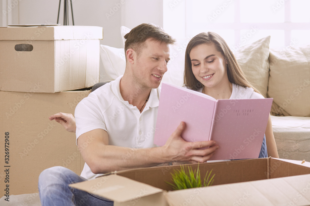 Portrait of happy couple looking at laptop computer together sitting in new house, surrounded with boxes Portrait of happy couple looking at laptop computer together sitting in new house, surrounded with boxes