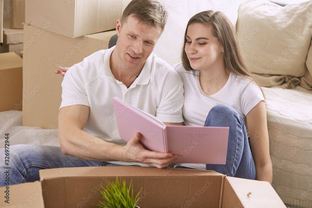 Portrait of happy couple looking at laptop computer together sitting in new house, surrounded with boxes Portrait of happy couple looking at laptop computer together sitting in new house, surrounded with boxes