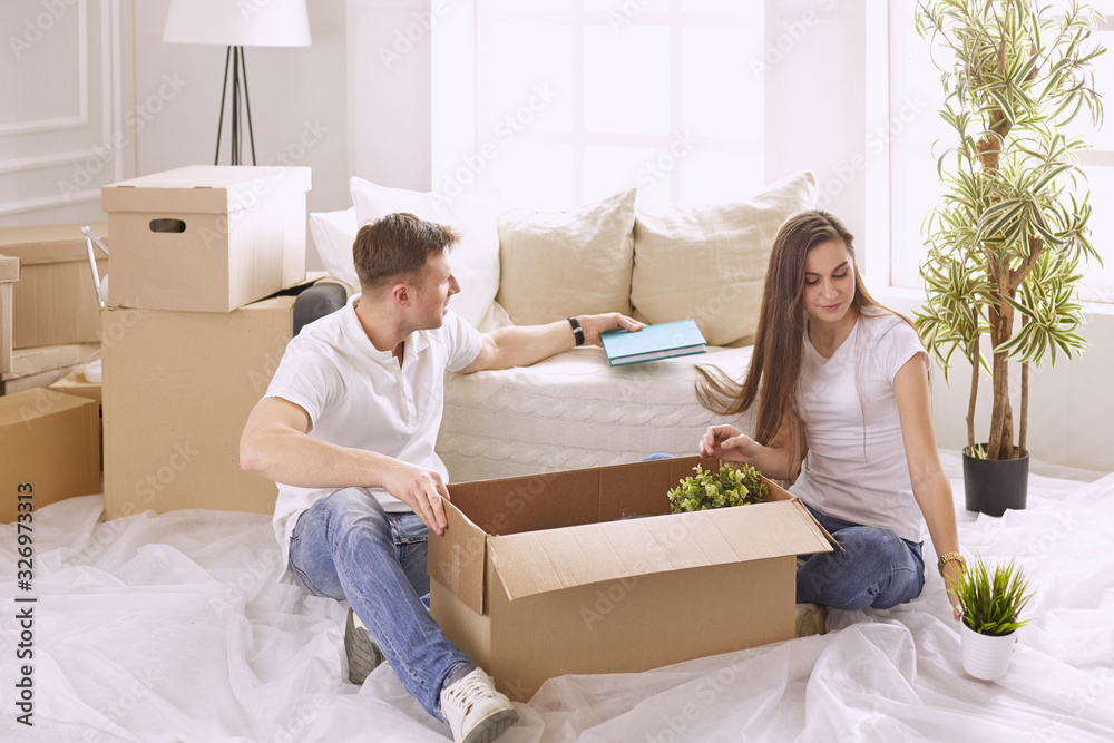 Portrait of happy couple looking at laptop computer together sitting in new house, surrounded with boxes