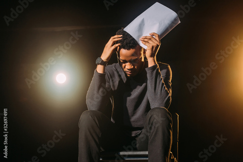 Fototapeta stressed african american actor holding scenario on stage during rehearse