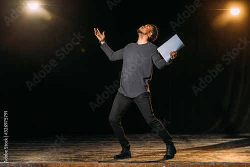 african american actor holding scenario and standing on stage during rehearse in theatre photo