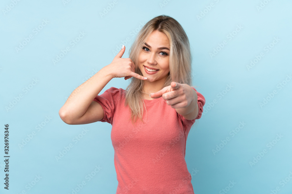 Fototapeta premium Teenager girl over isolated blue background making phone gesture and pointing front
