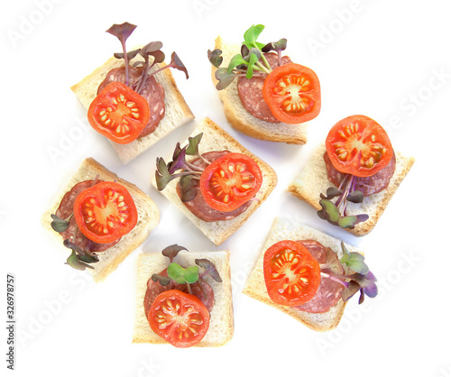 Small sandwiches, finger food, with sliced salami, tomatoes and micro greens radish isolated on white background. Pieces of bread with sausage and vegetables top view..