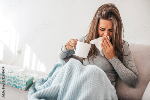 Sick woman with headache sitting under the blanket in living room. Sick Woman Covered With a Blanket Lying in Bed With High Fever and a Flu, Resting at Living Room.