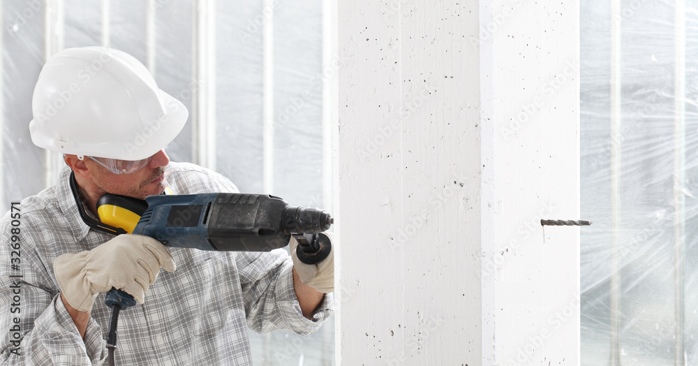 man using an electric pneumatic drill making a hole in wall, professional construction worker with safety hard hat, hearing protection headphones, gloves and protective glasses. man using an electric pneumatic drill making a hole in wall, professional construction worker with safety hard hat, hearing protection headphones, gloves and protective glasses.
