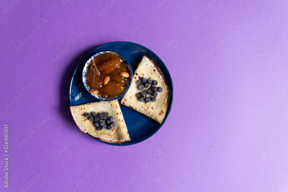 Pancake with blueberries, apricot jam with nuts in bowl on purple background Pancake with blueberries, apricot jam with nuts in bowl on purple background
