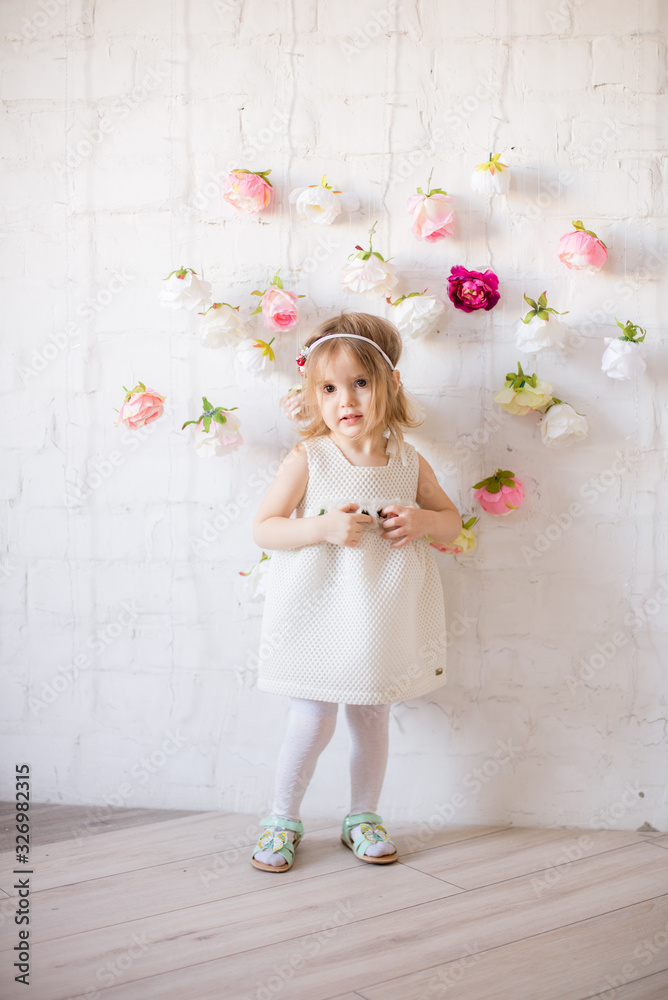 Little cute girl in a beautiful white dress in a spring light studio ...