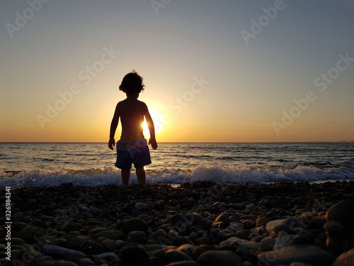 a little boy watching the sunset at the beach.