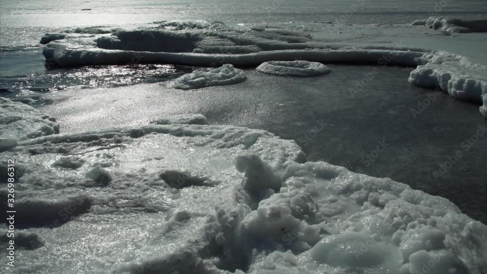 Shore covered with white ice under bright spring sun and ice floes floating in water