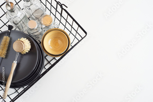 Basket with kitchen utensils  plates  glass bottles  a granny brush for washing dishes  towels on white background. Zero Waste concept. Top view