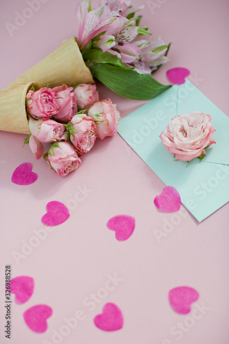 Ice cream cones with pink flowers and mint envelope on pink pastel background with heart shaped confetti