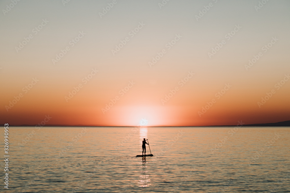 Woman paddling on a board on the sea in sunset