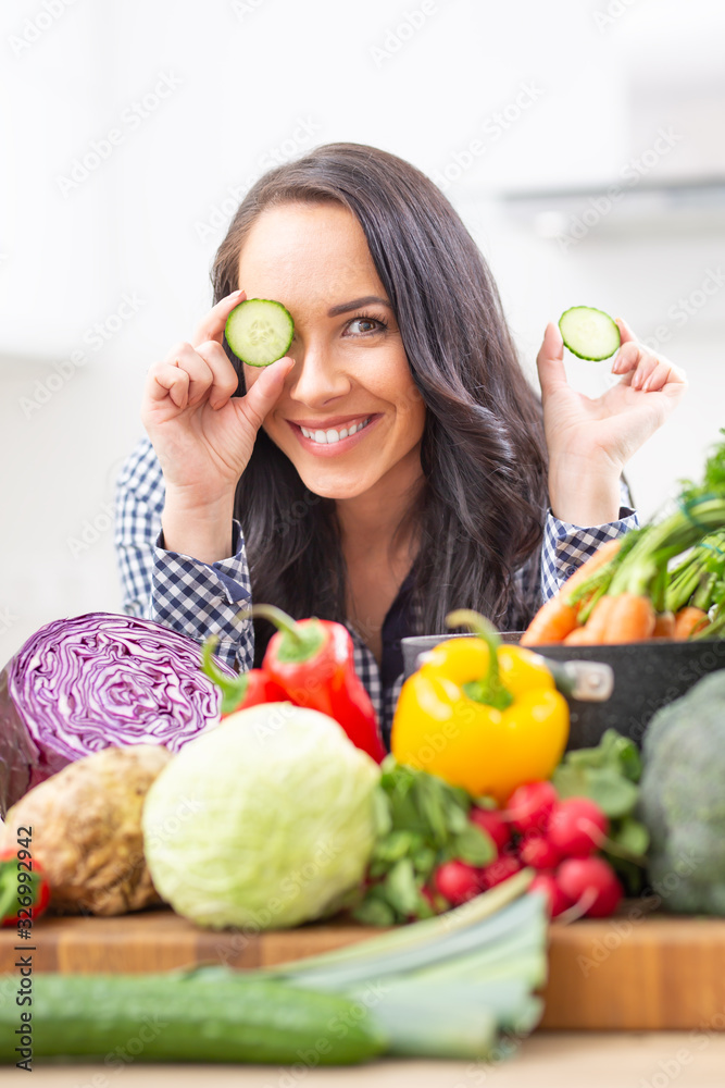 Cheerful young woman holding slices of cucumber in the kitchen - diet vegetable and heath concept Cheerful young woman holding slices of cucumber in the kitchen - diet vegetable and heath concept